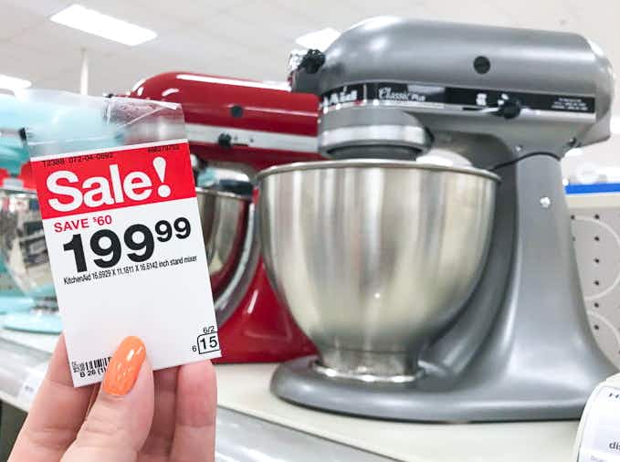 a silver kitchenaid stand mixer on the shelf at target with a woman's hand holding a sale tag next to it that reads $199.99