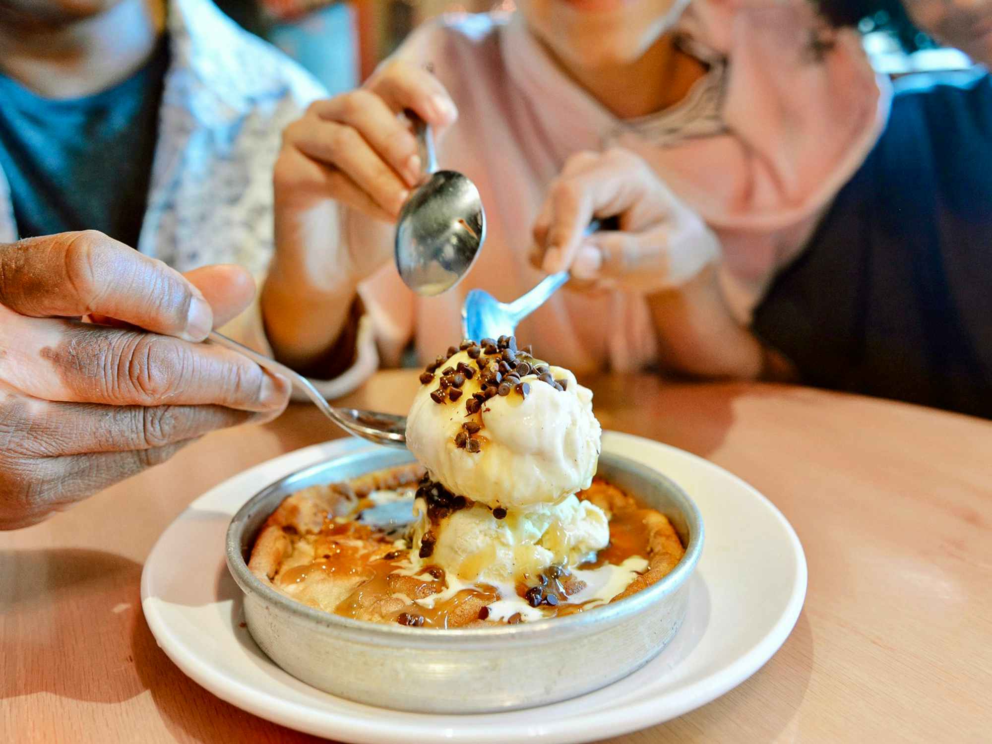 three people digging their spoons into a pizookie from bjs restaurant and brewhouse