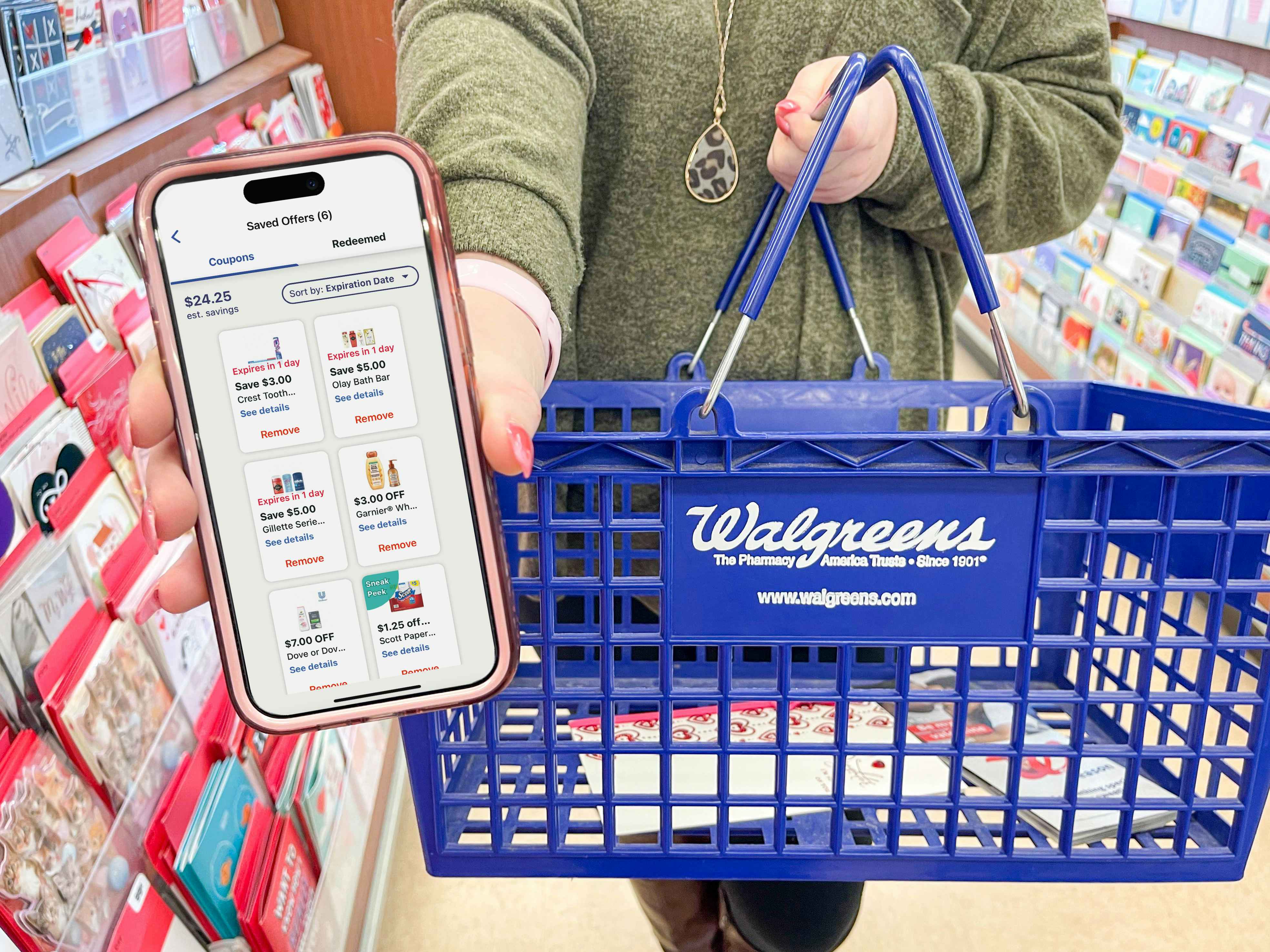 Someone holding a phone displaying the coupons in the Walgreens app and holding a Walgreens shopping basket