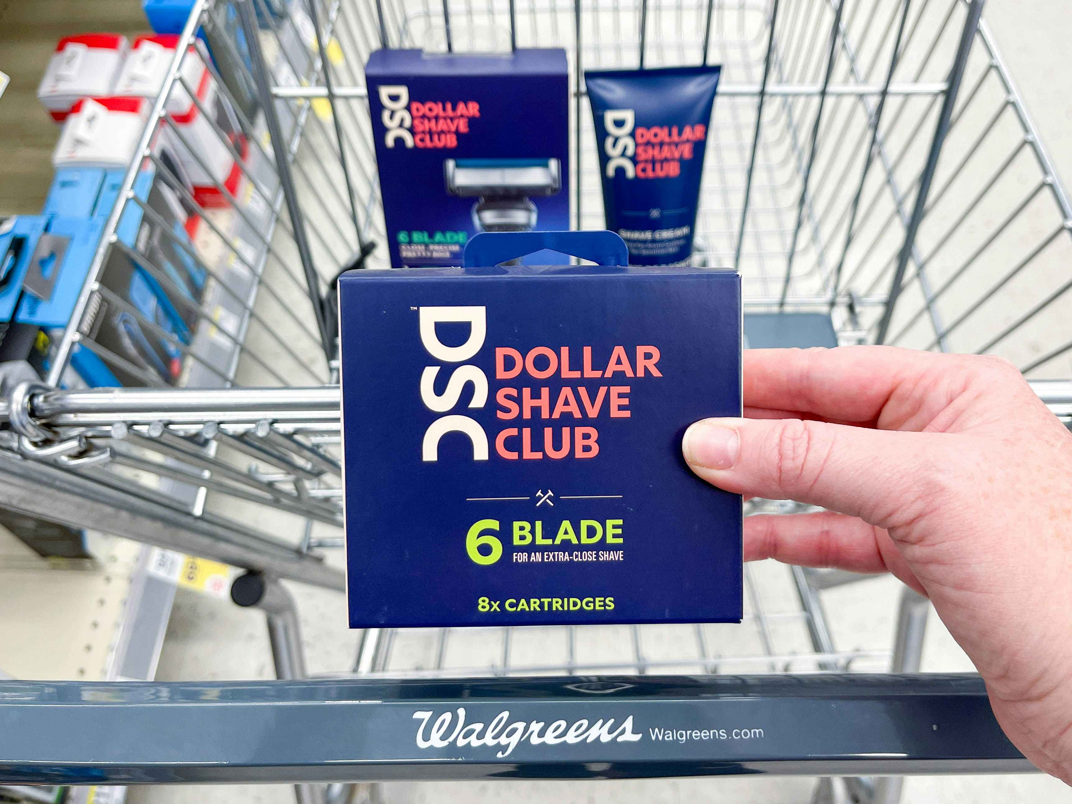 Dollar Shave Club razors and blades boxes in a Walgreens cart with razors being held in front 