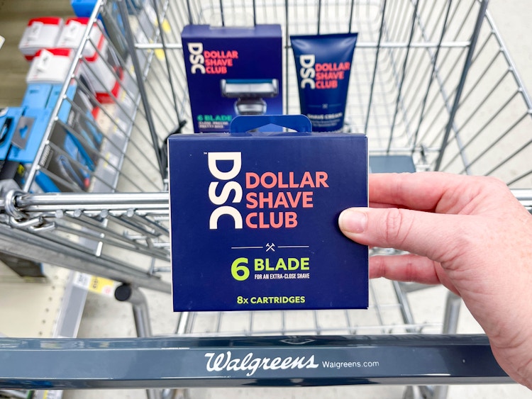 Dollar Shave Club razors and blades boxes in a Walgreens cart with razors being held in front 
