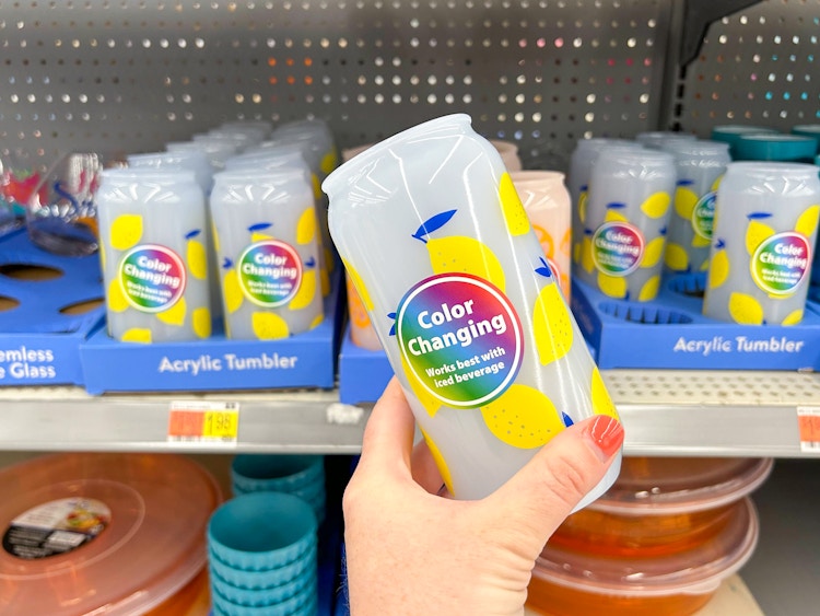 a woman holding a blue color changing tumbler can in front of others on the shelf at Walmart