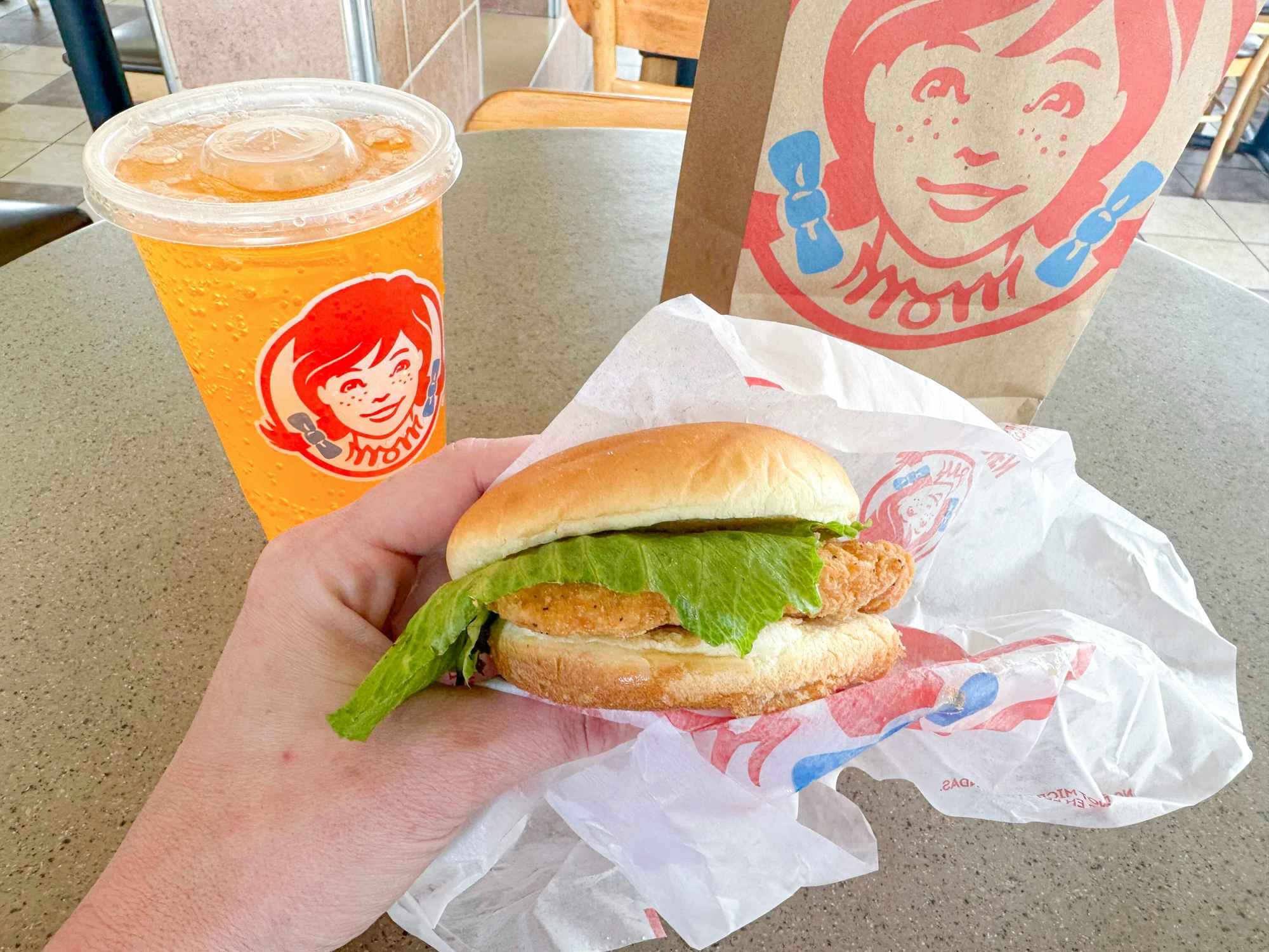 Someone holding a Crispy Chicken Sandwich at Wendy's in front of a drink and bag