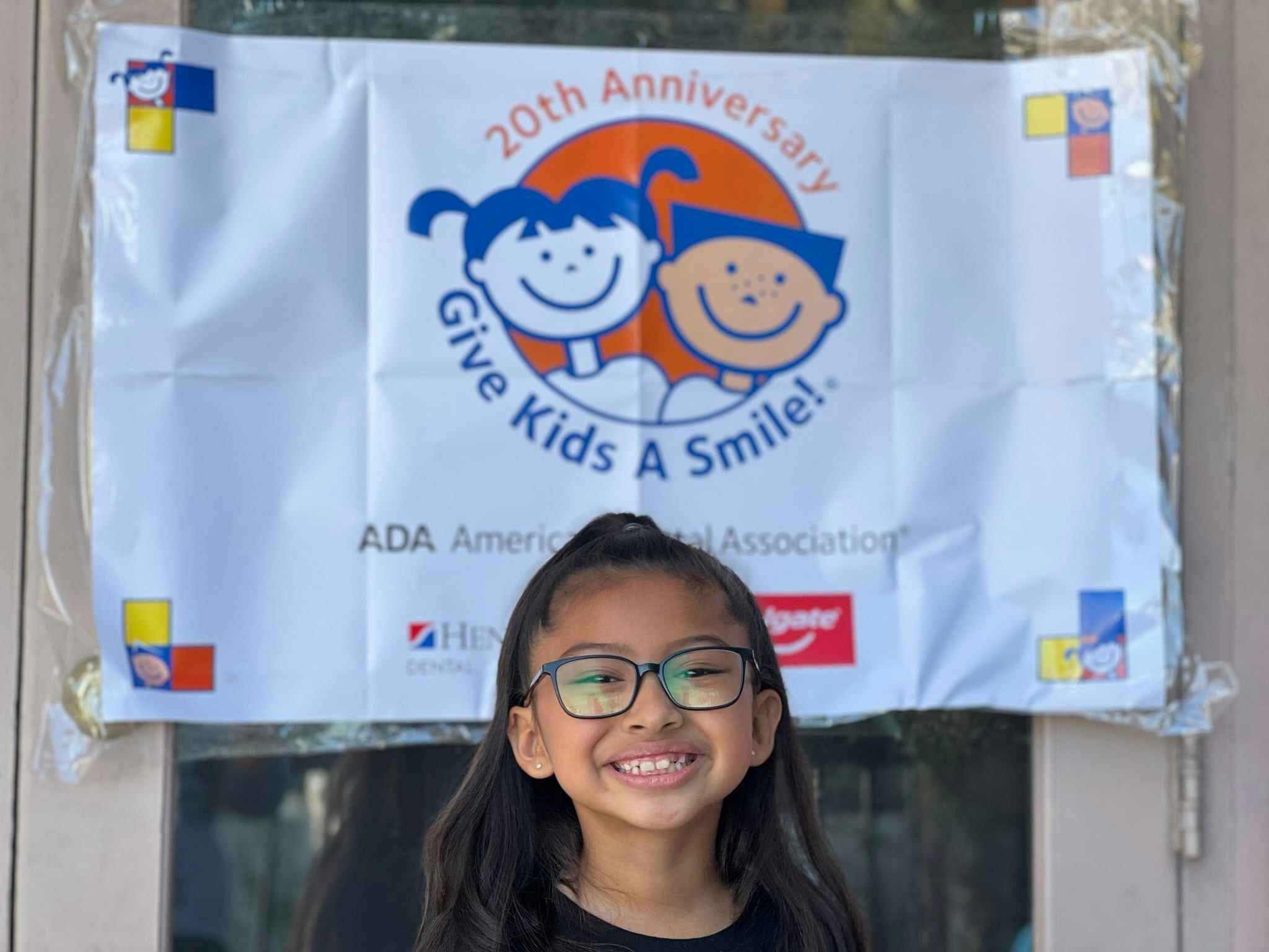 A child smiling in front of a Give Kids a Smile sign