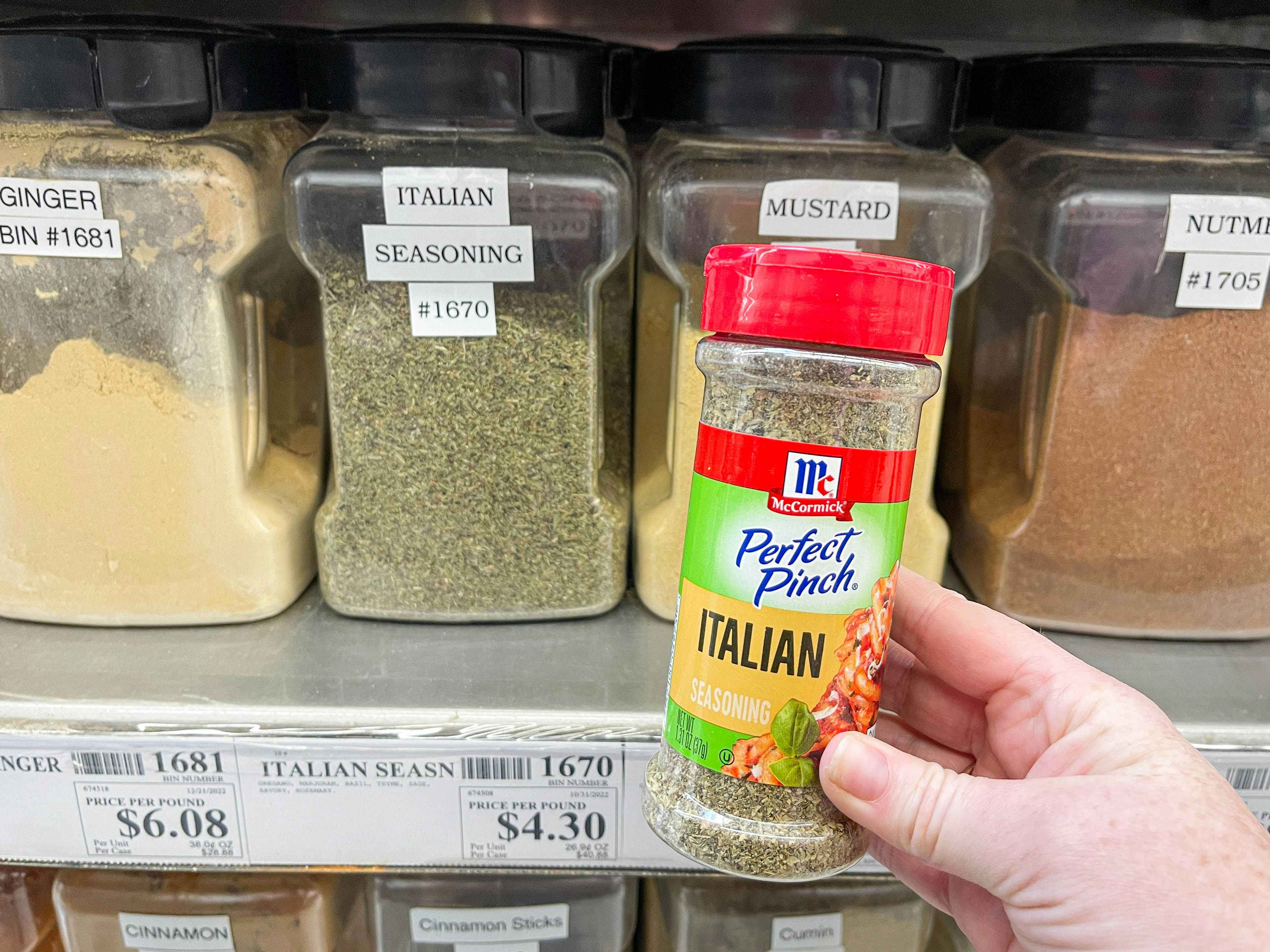 a bottle of itallian seasoning being held in fromt of winco bulk spices