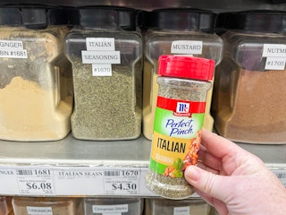 a bottle of itallian seasoning being held in fromt of winco bulk spices
