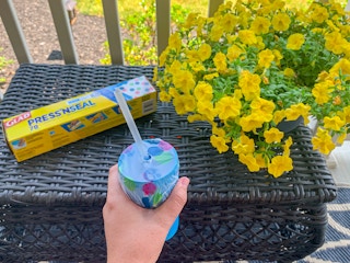 a person holding up a sippy cup with a GLAD seal on top of it