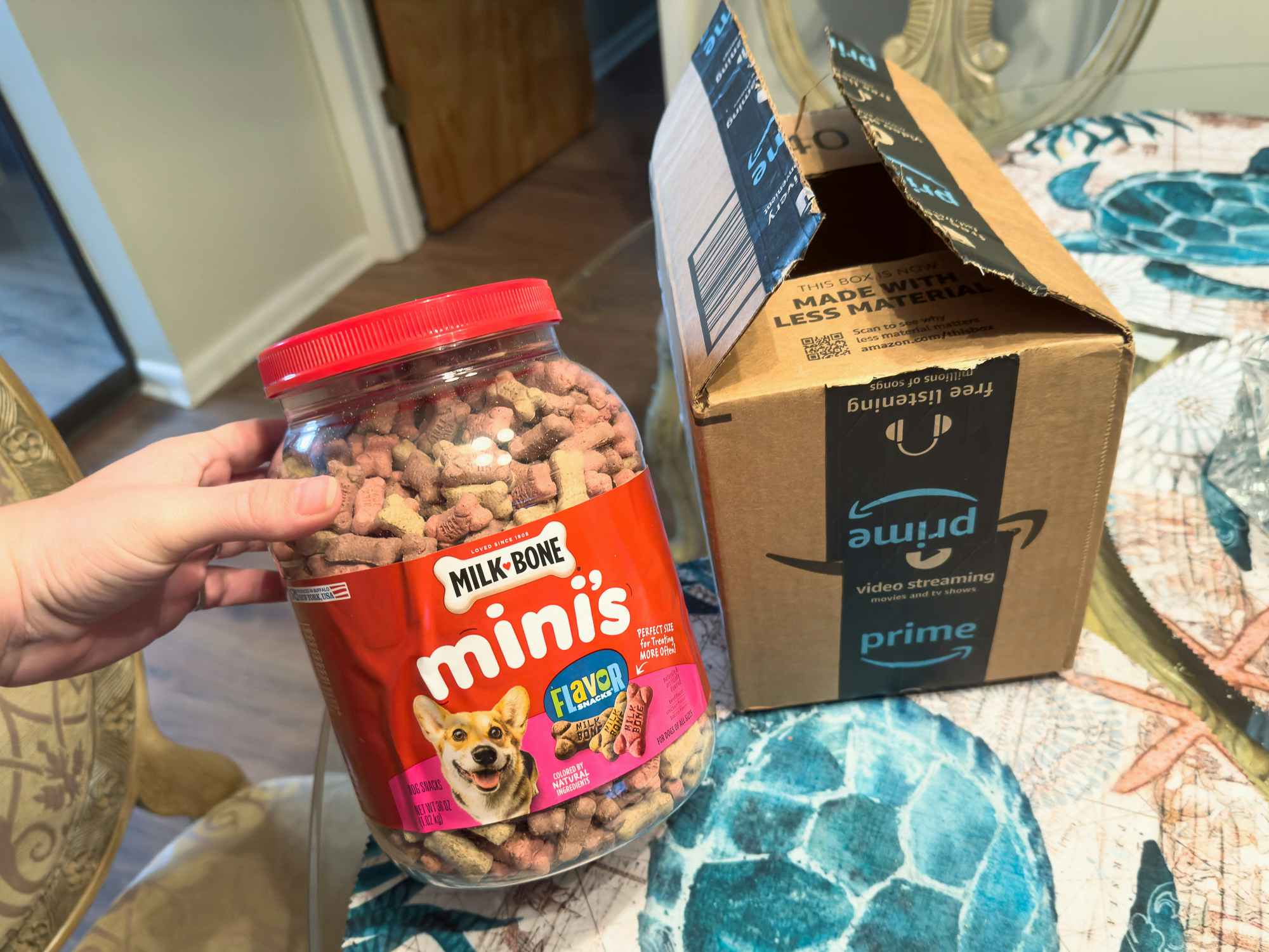 Someone holding a tub of Milkbone Mini dog treats next to an Amazon box