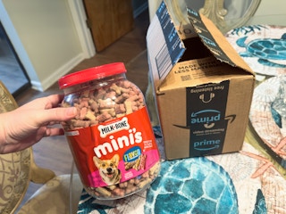 Someone holding a tub of Milkbone Mini dog treats next to an Amazon box