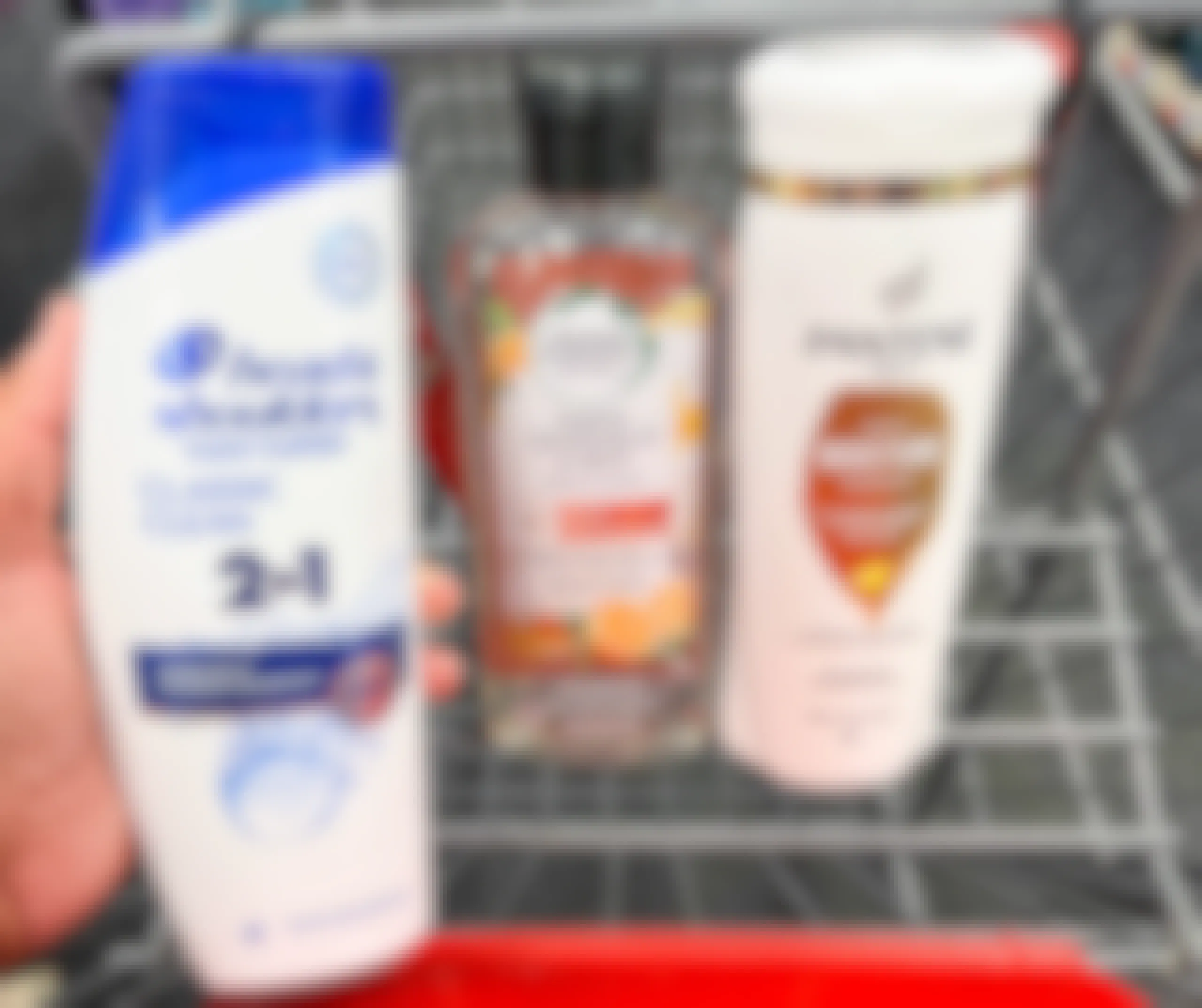 hand holding one bottle of head & shoulders shampoo, herbal essences shampoo, and Pantene shampoo in shopping cart