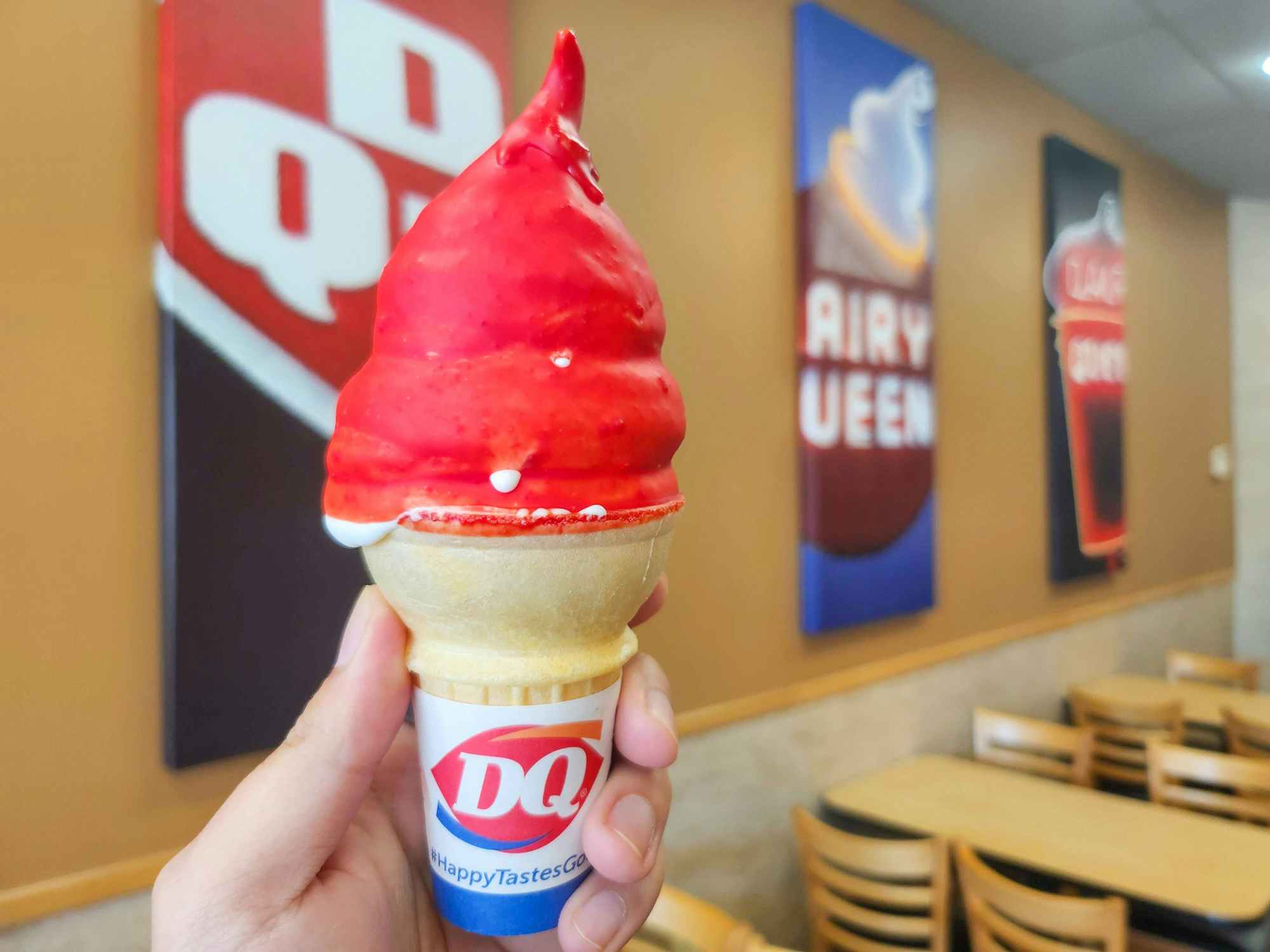 Someone holding up a cherry dipped ice cream cone at Dairy Queen