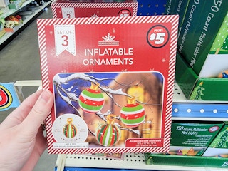 Hand holding a box of Dollar Tree Plus inflatable ornaments.