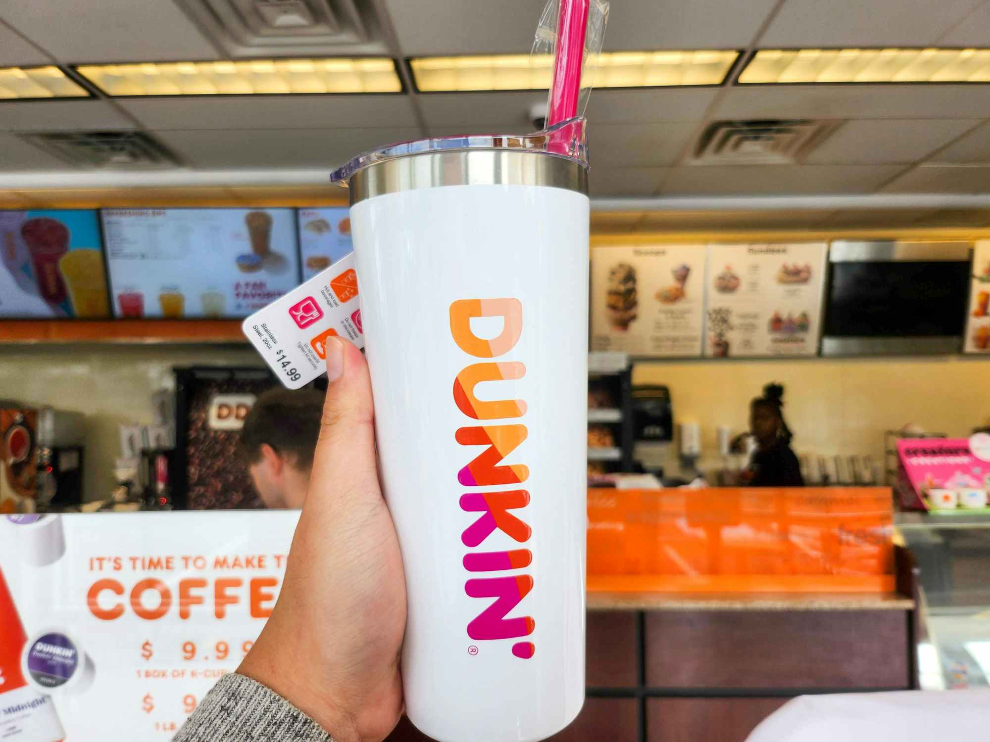 Someone holding up a Dunkin tumbler with a straw