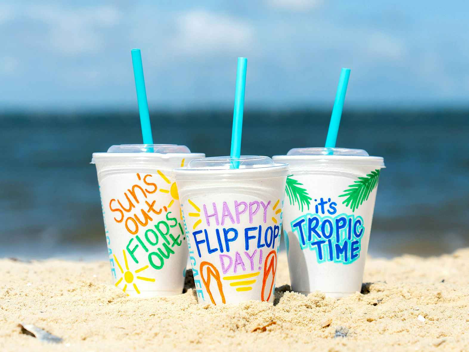 three tropical smoothie cups for flip flop day on a beach