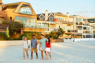 Four people walking together on a beach with homes in the background