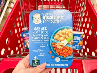 A Gerber Mealtime for toddler meal held out by hand in front of a store cart with other Gerber items in it.