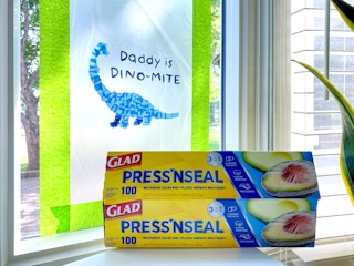 art project using glad press'n seal on a window with a dinosaur made of tissue paper