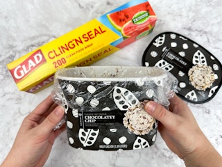 Someone using Glad Cling N' Seal to prevent freezer burn on a tub of ice cream