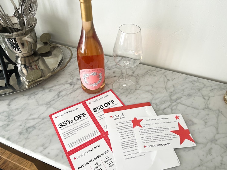 A bottle of wine on a counter with some Macy's Wine Shop coupons and information cards