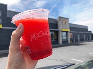 a person holding a mcdonalds slushie in front of a mcdonalds