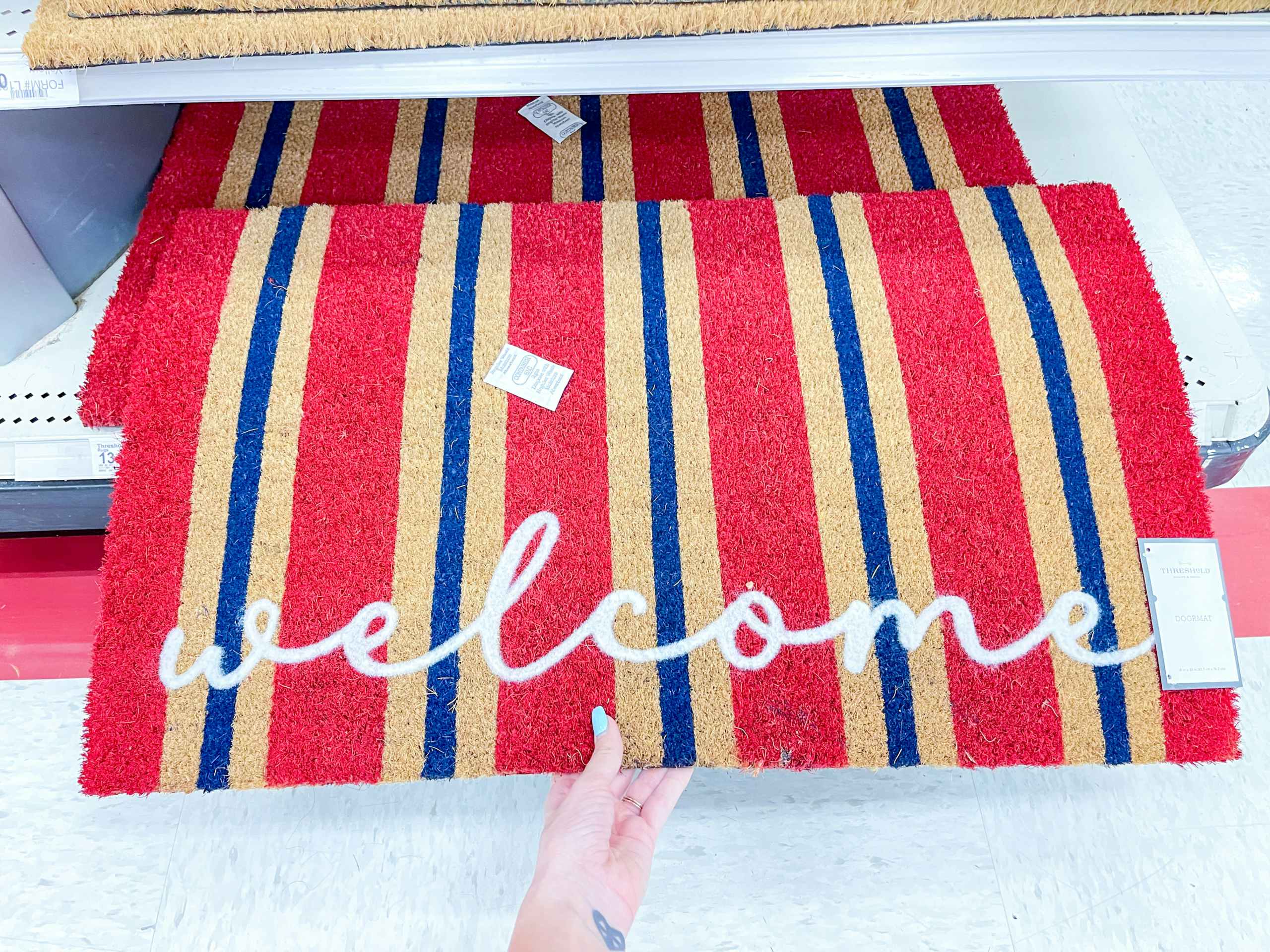 A welcome Mat held out by hand slightly off the store shelf