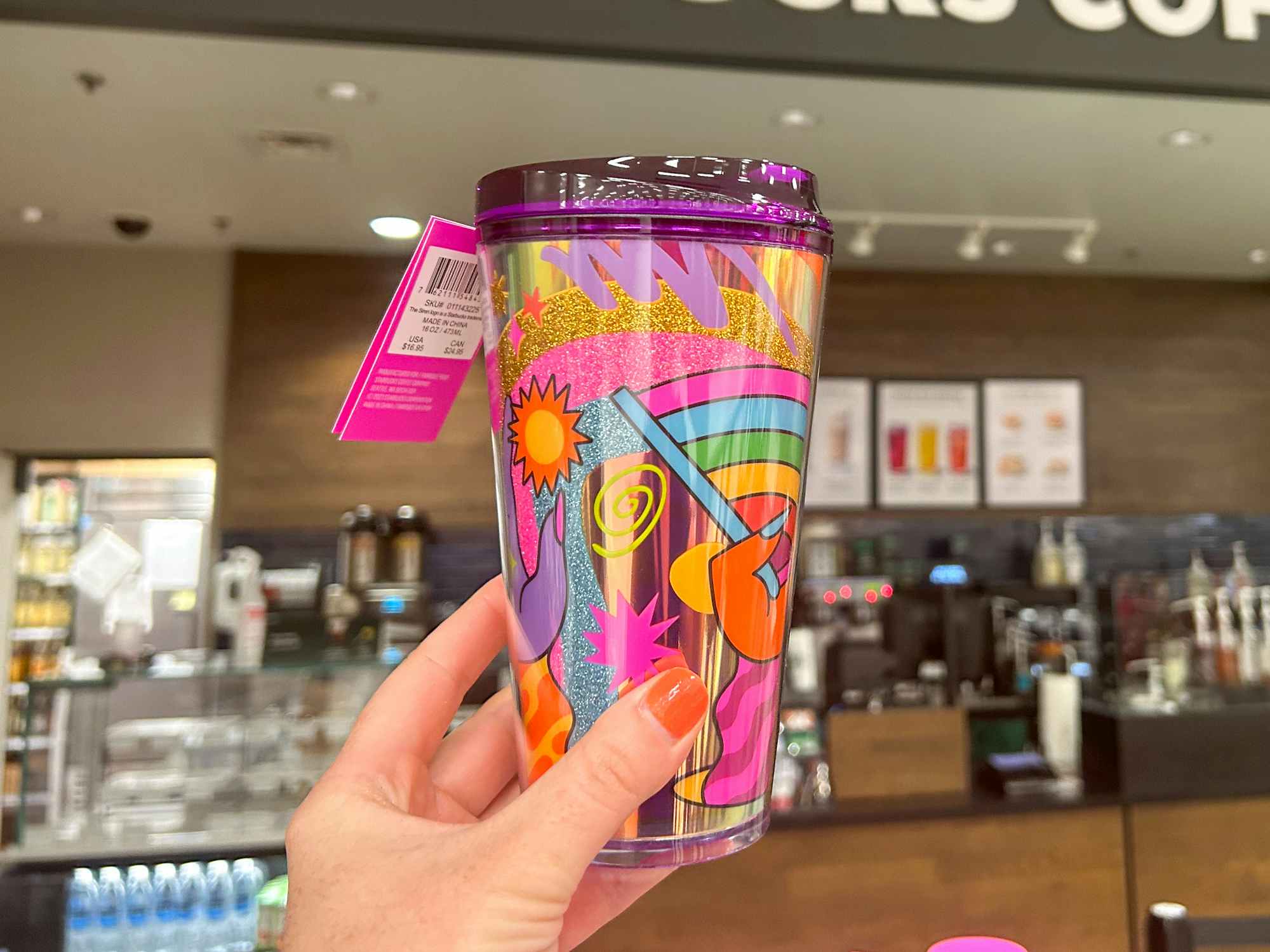 Someone holding up a Starbucks Pride cup inside a Starbucks