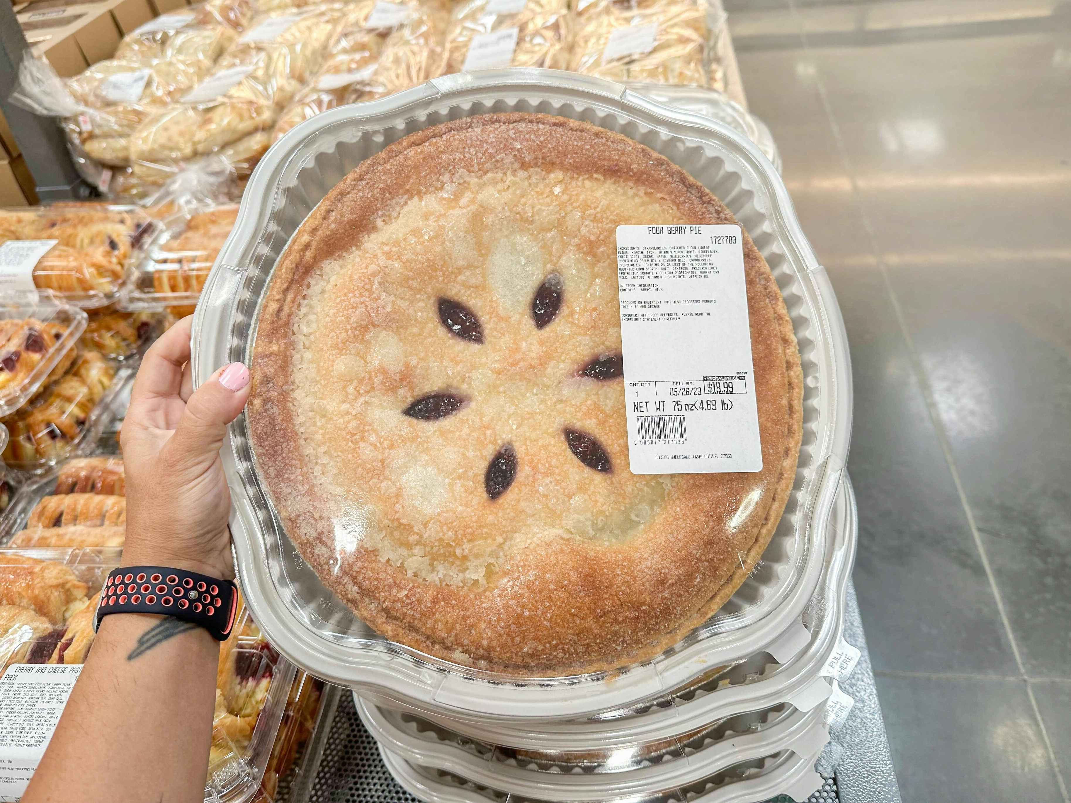 a person holding up a four berry pie at costco