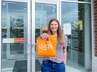 A person holding up a bag of items purchased from Ulta in front of an Ulta store
