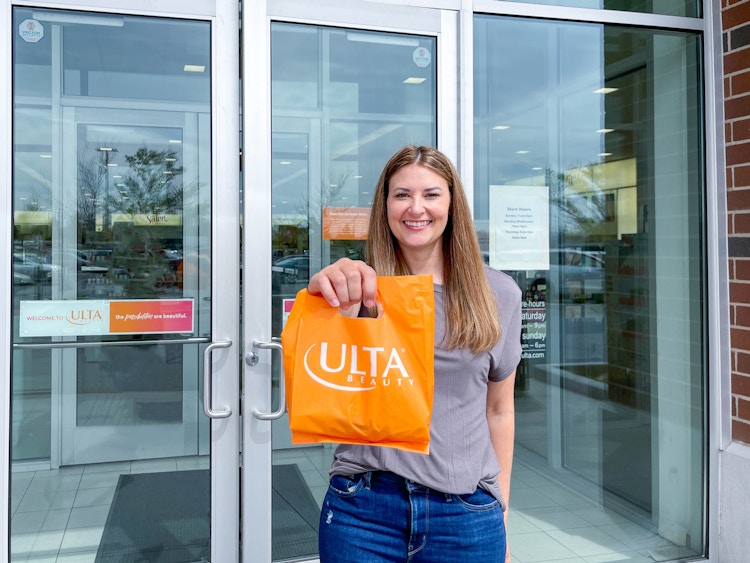A person holding up a bag of items purchased from Ulta in front of an Ulta store