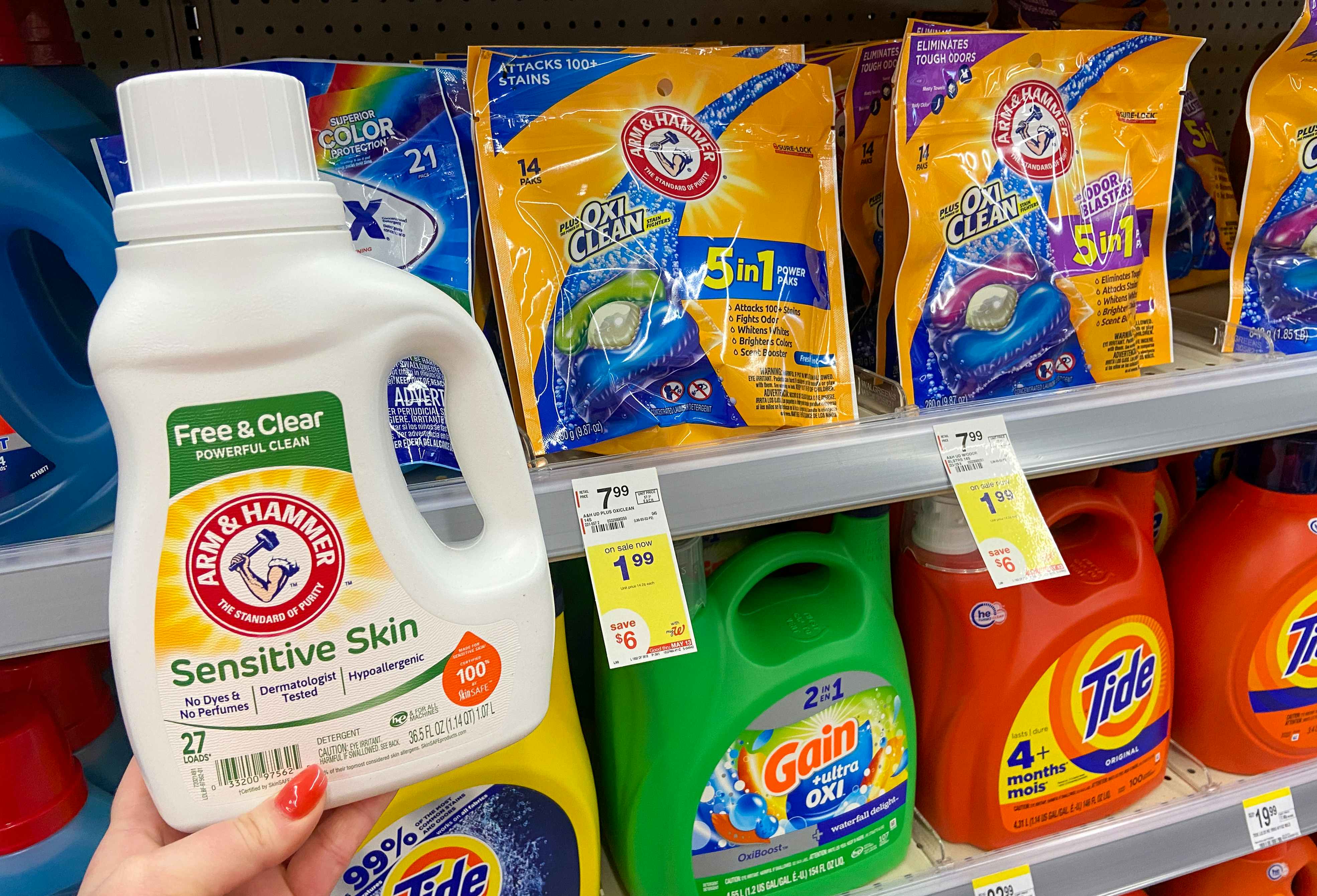 hand holding arm and hammer laundry detergent in front of a shelf with sale tags