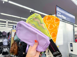 a person holding up three belt bags from walmart