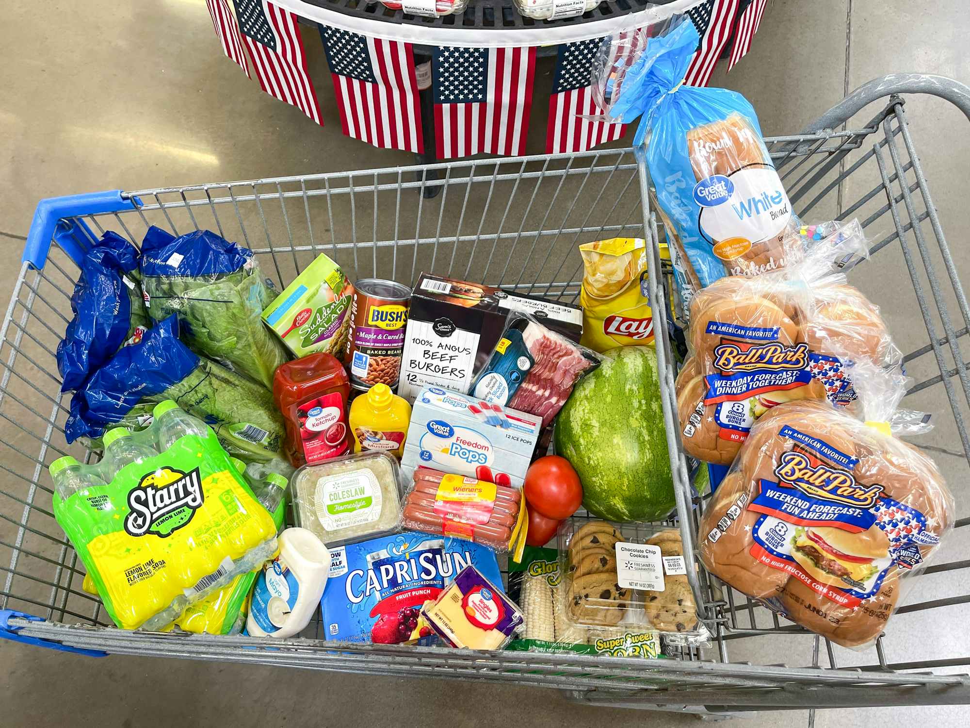 A cart filled with grilling essentials parked in front of some americana decor at Walmart