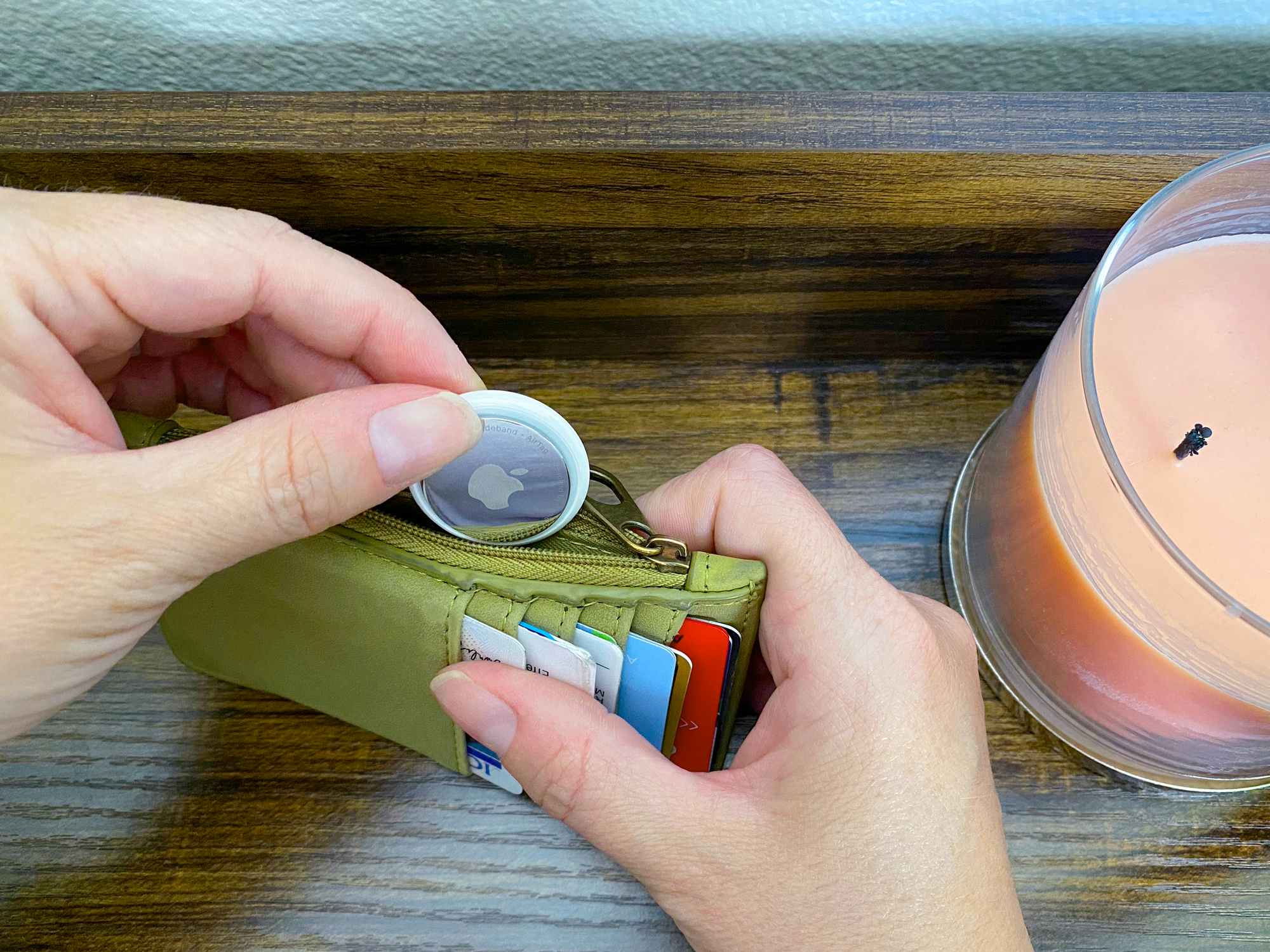 person placing an apple airtag inside zipper pocket of wallet for tracking