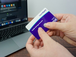 Someone holding an HSA card by a laptop