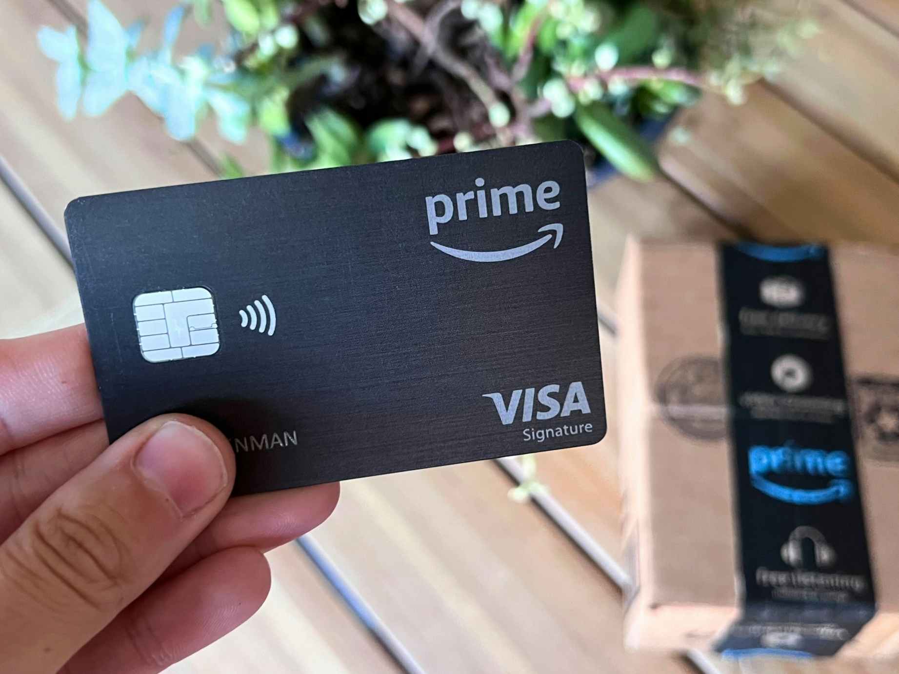 Someone holding an Amazon Prime credit card next to an Amazon box