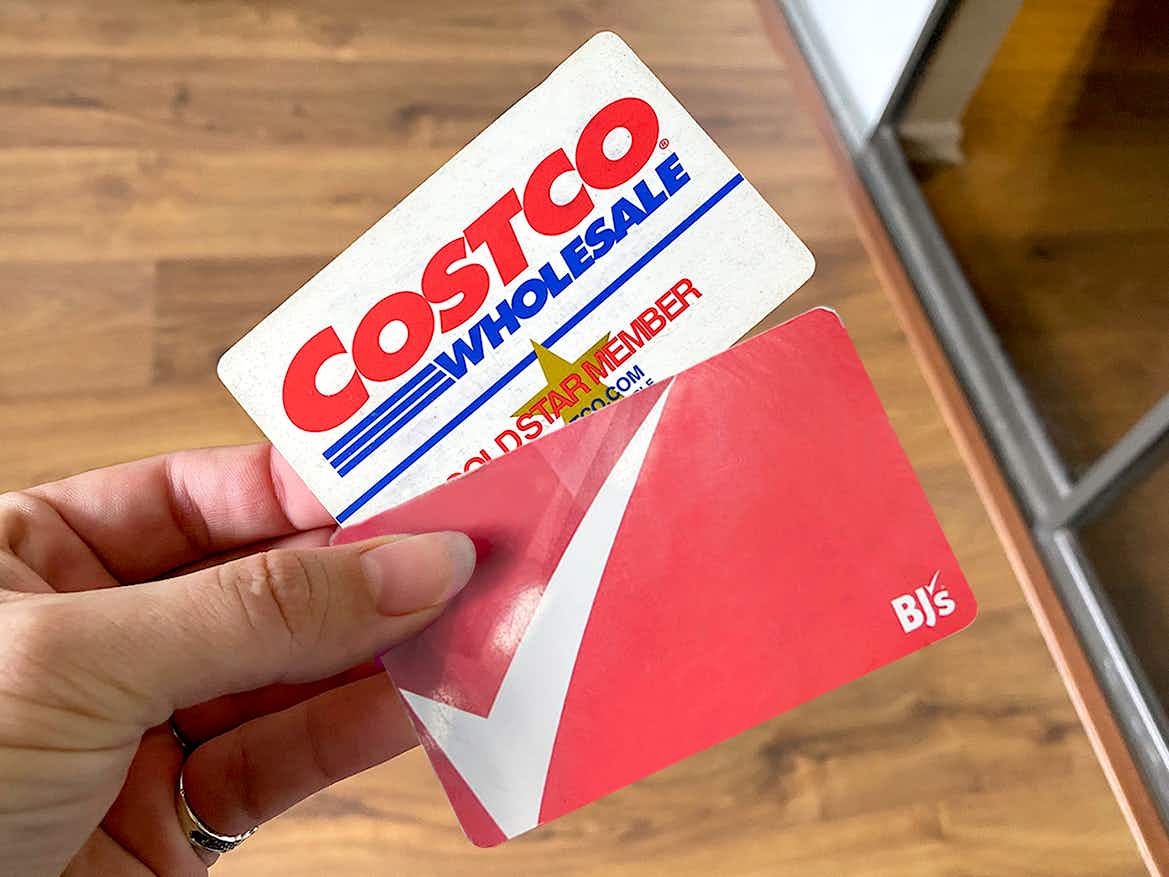person's hand holding costco gold and bj's club membership cards