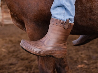 Someone riding a horse wearing a pair of Classic Western Boots from the Croc and Huckberry collab