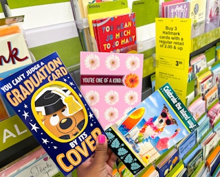 hand holding three Hallmark greeting cards next to sales tag and card display