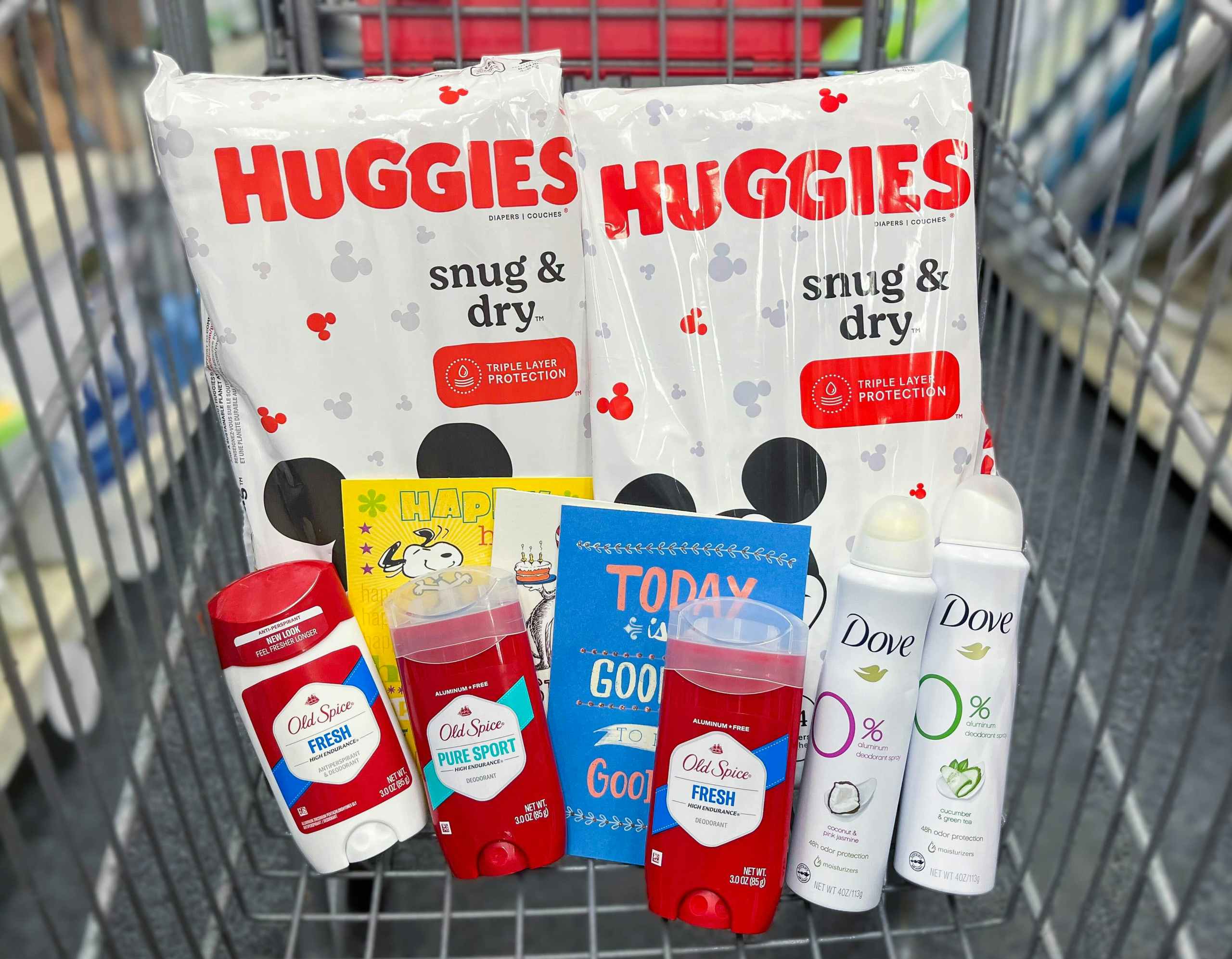 two packs of Huggies snug and dry diapers, three Old Spice deodorants, two Dove dry sprays, and three Hallmark cards inside shopping cart