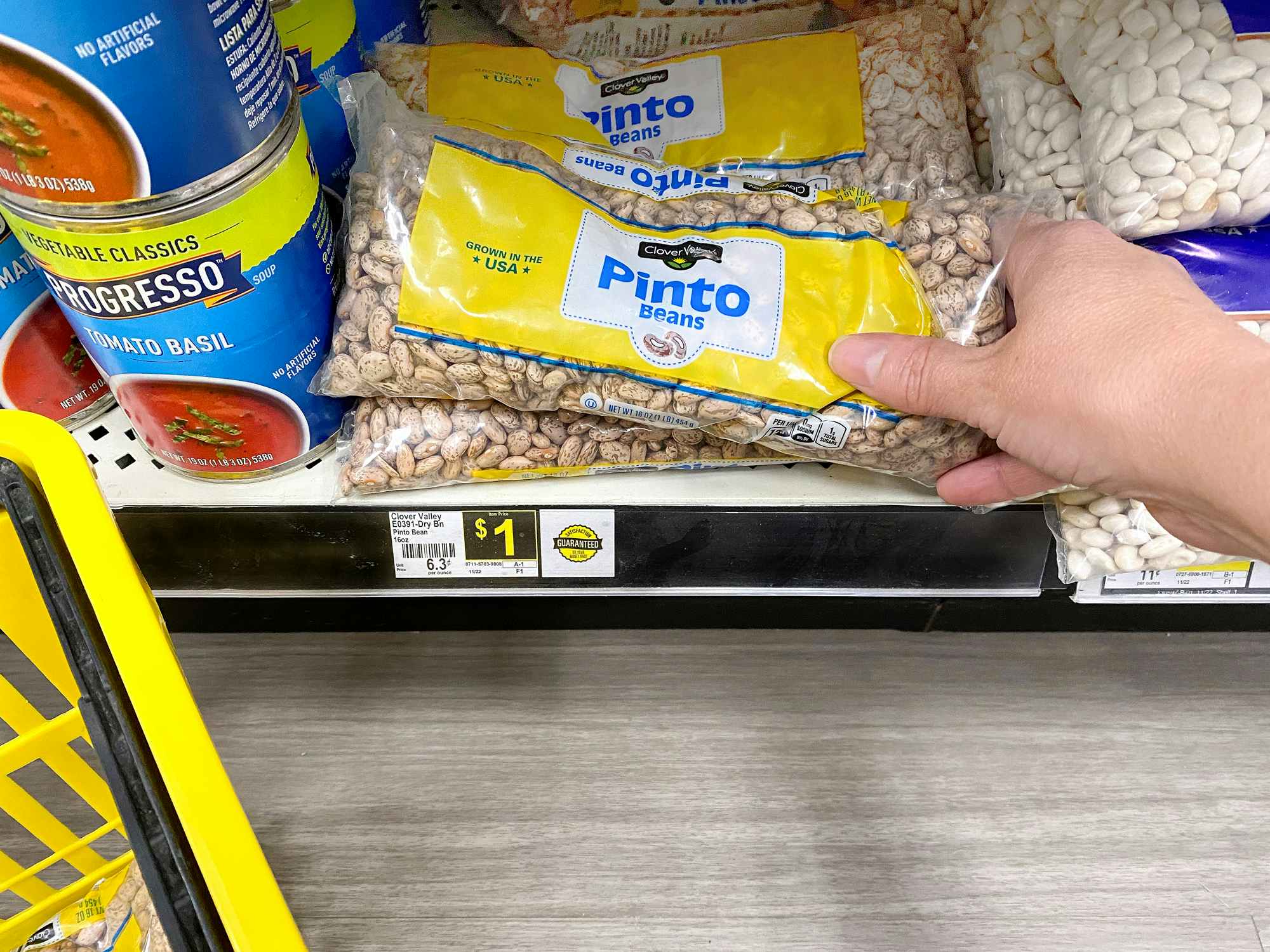 person grabbing a 16 ounce bag of dry pinto beans from a dollar general shelf for one dollar
