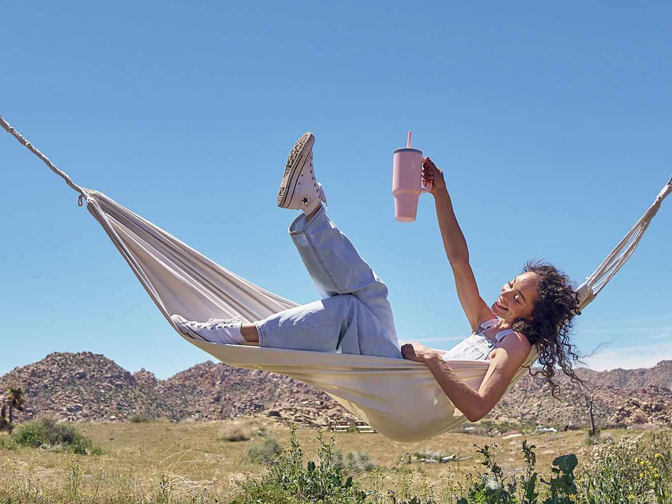 A person lounging in a hammock holding up a Hydro Flask All Around Travel Tumbler
