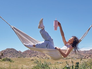 A person lounging in a hammock holding up a Hydro Flask All Around Travel Tumbler