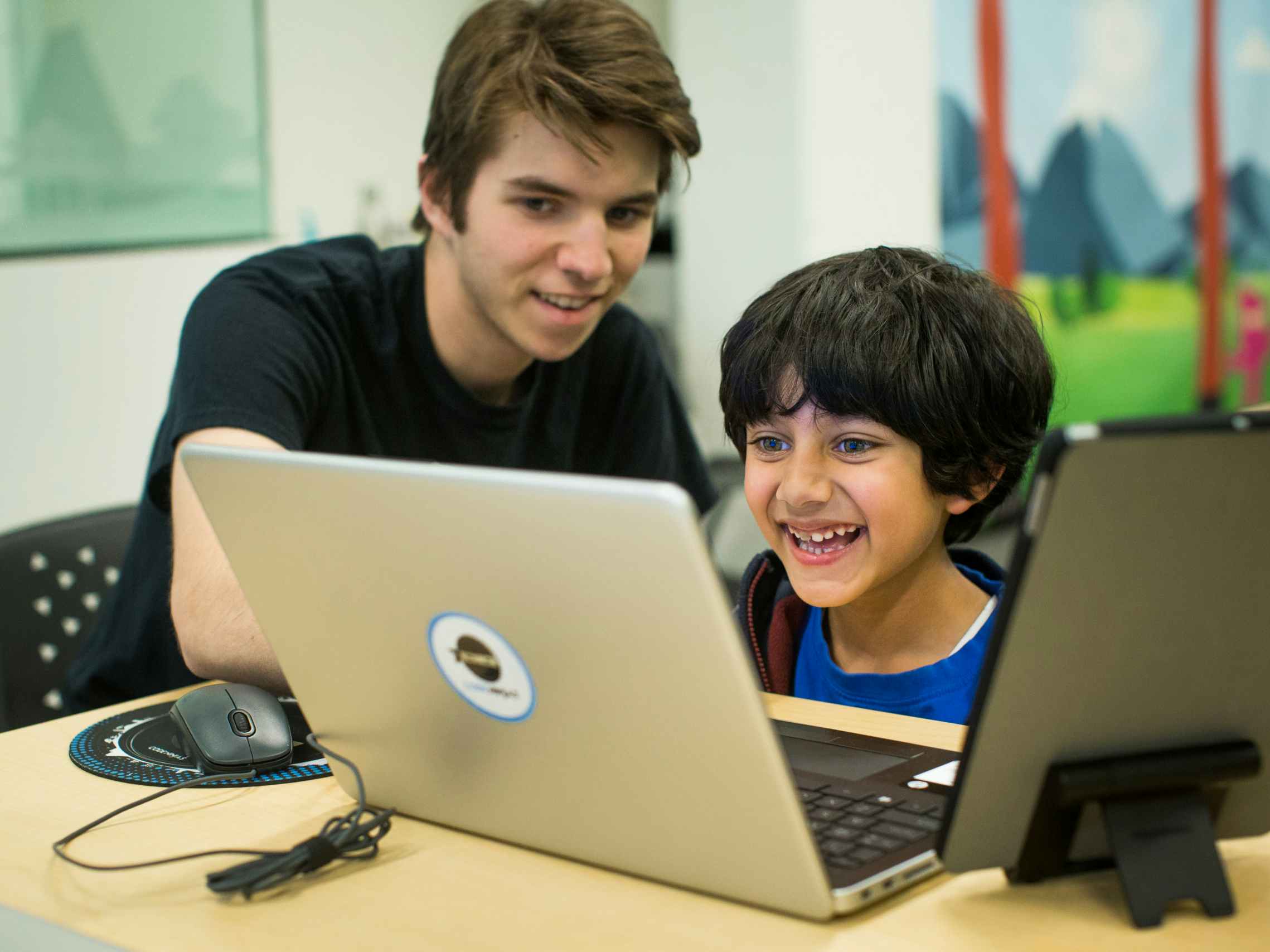 A child working on a laptop with an adult sitting next to him watching the screen