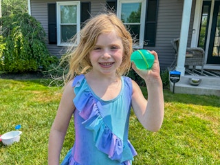 a child smiling while holding a reusable water balloon