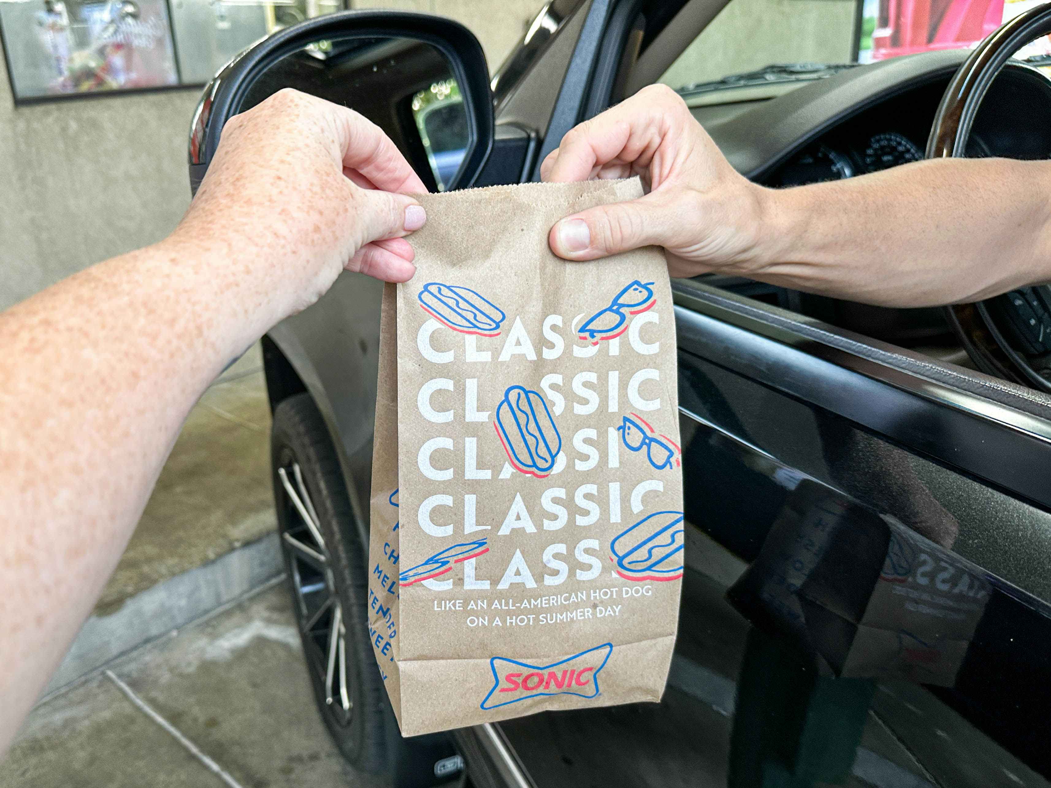 a person handing a sonic bag to a person to a person sitting in a car