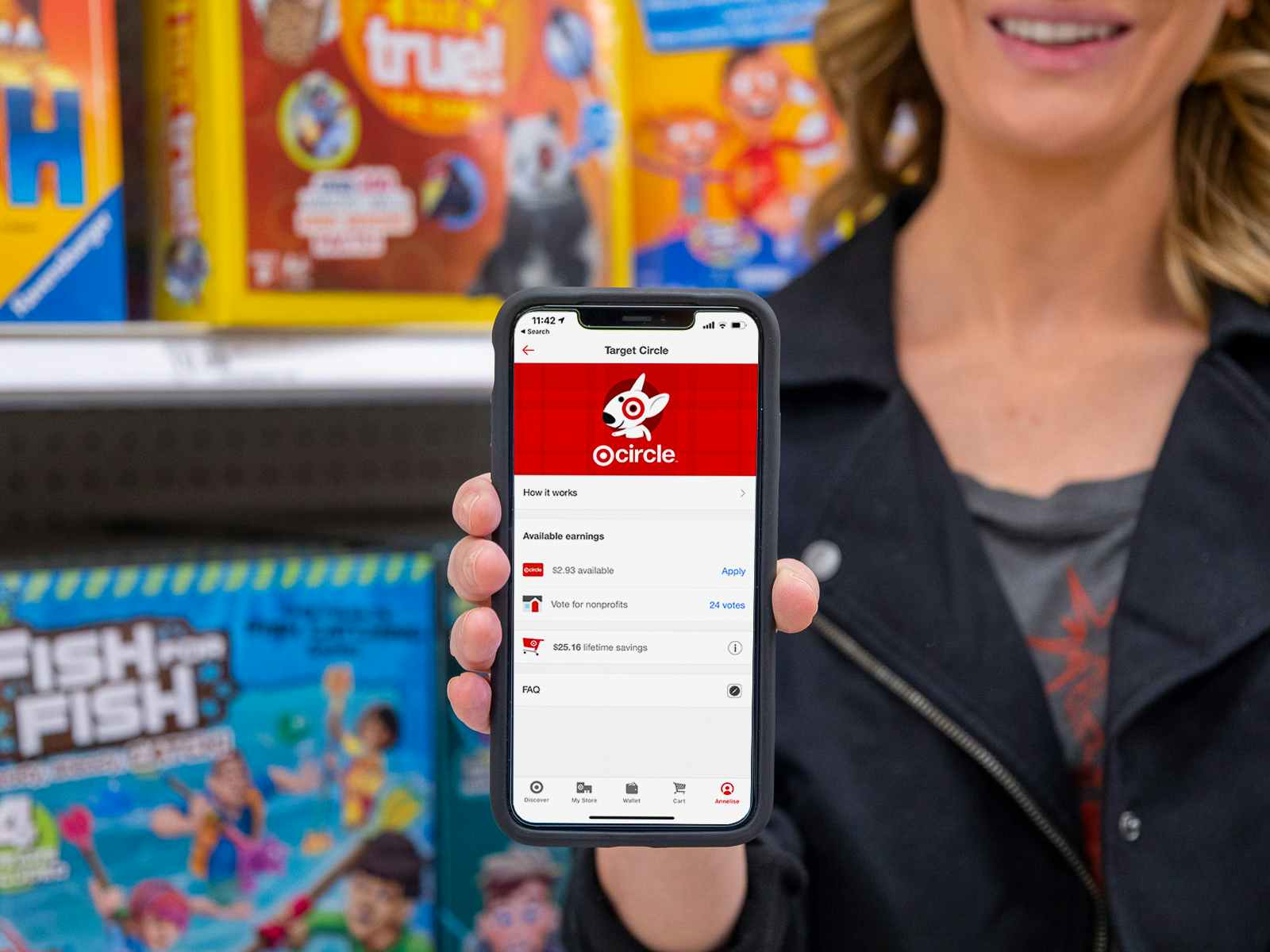 A woman standing in front of toys on a shelf and holding up her phone, showing her Target Circle account info in the Target app