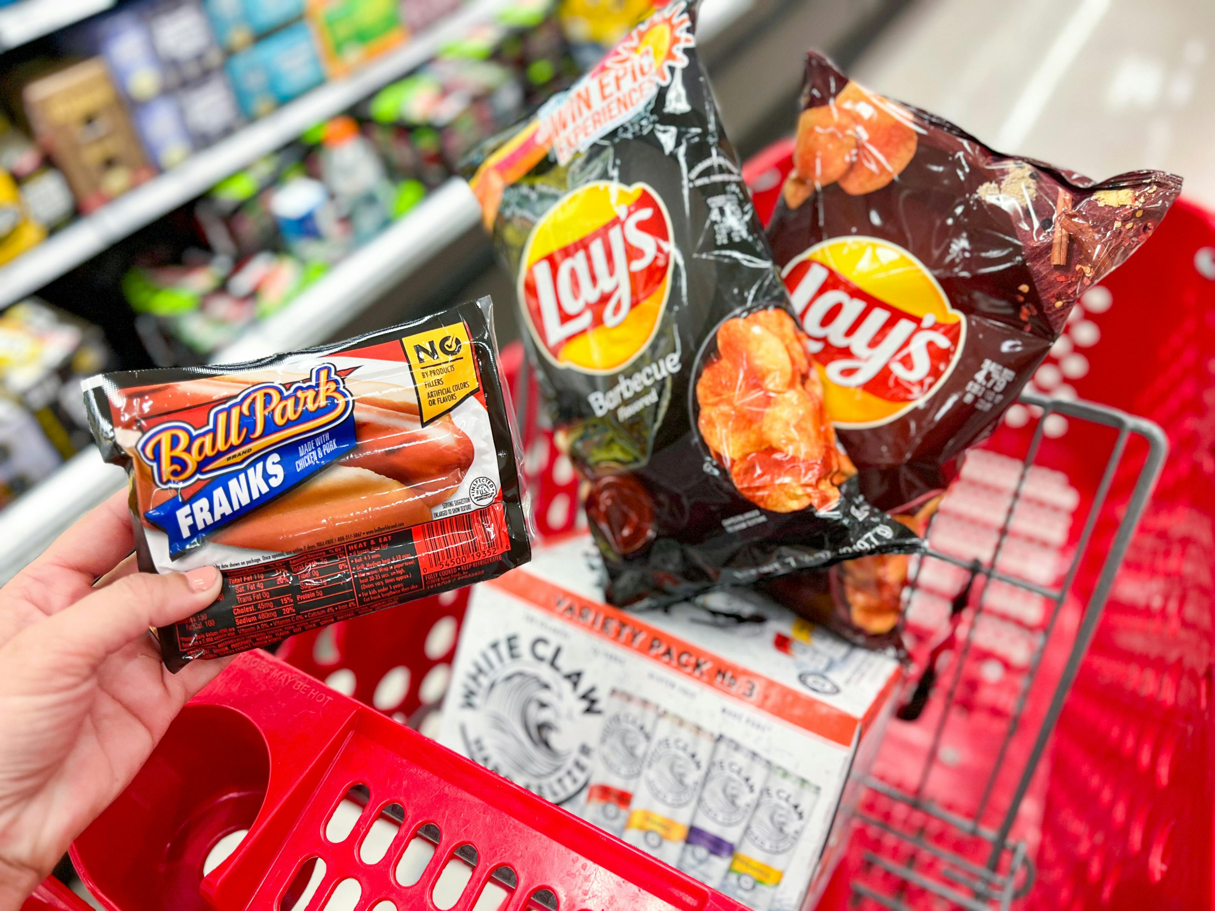 a person putting a package of hot dogs into a target cart next to bags of chips