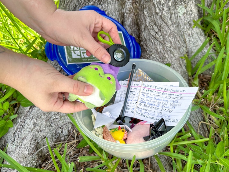 Someone placing a Travel Bug with an Airtag into a Geocache tupperware