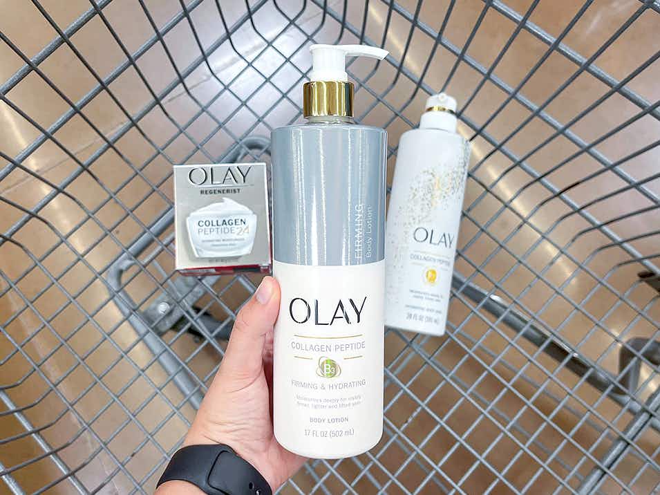 person holding olay collagen peptide firming body lotion alongside other olay products in walmart cart