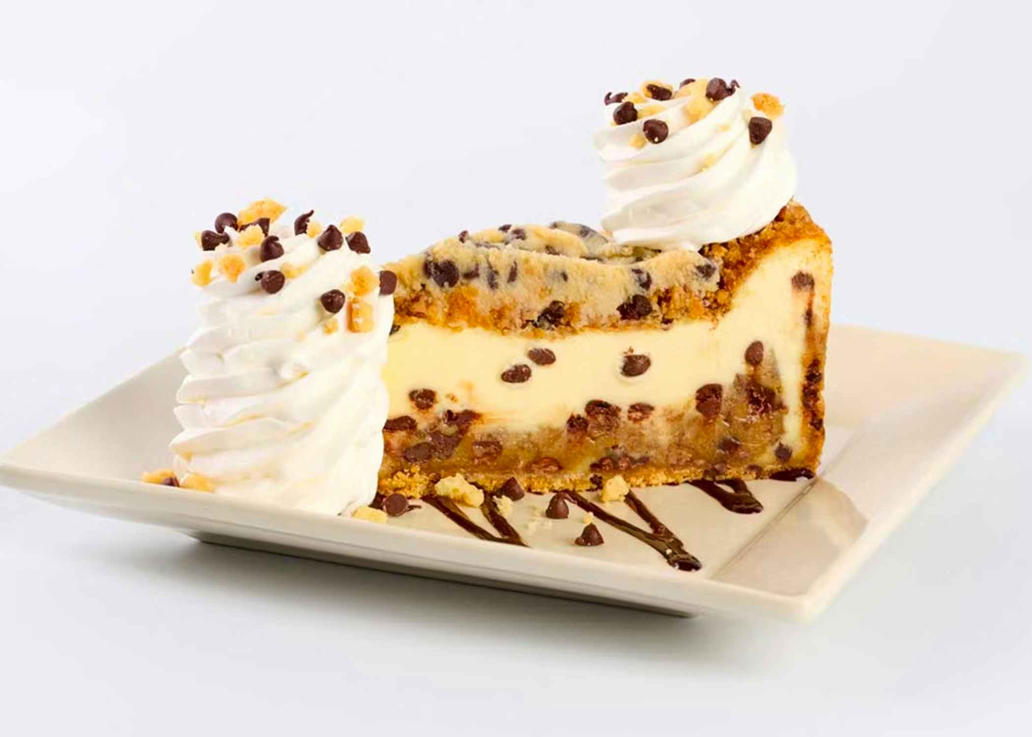 a slice of cookiedough and pecan flavored cheesecake with dollops of whip cream on a white plate